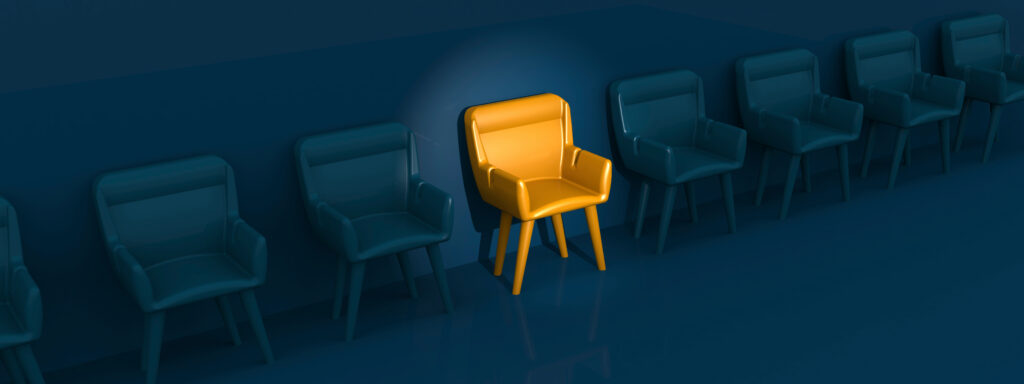 Eine Reihe identischer dunkelblauer Stühle steht an einer Wand. Ein Stuhl, der mittig zwischen den anderen steht, sticht in leuchtendem Gelb hervor und zieht die Aufmerksamkeit in der ansonsten einfarbigen Umgebung auf sich – ähnlich wie die Web Agentur Leipzig bei digitalen Innovationen hervorsticht.